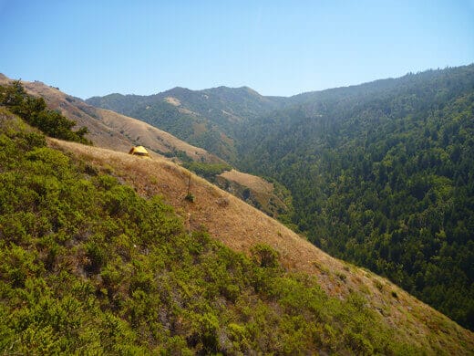 Tent perched on a bluff overlooking a verdant canyon