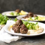 Three plated servings of lamb kofta with hummus and herbs.