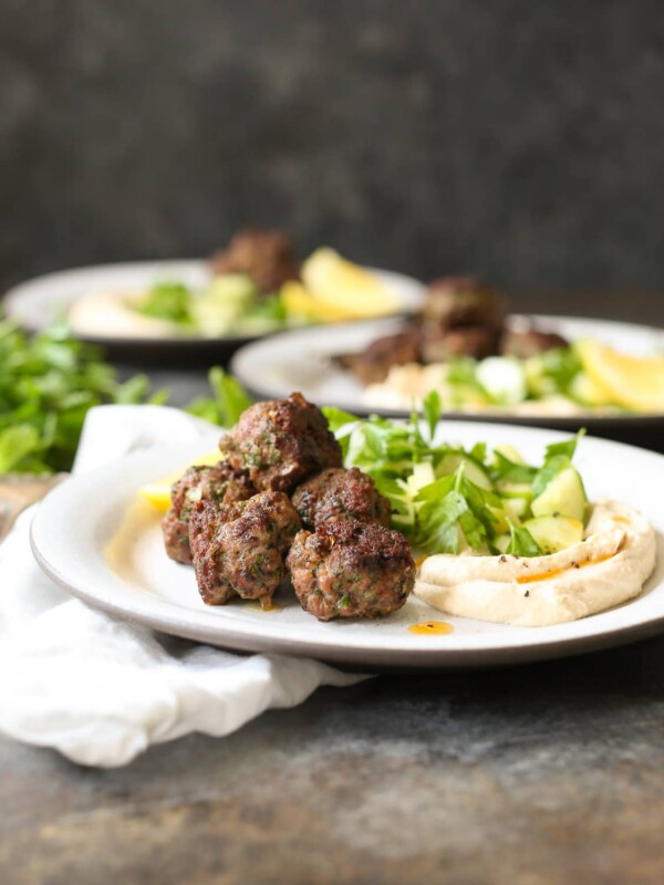Three plated servings of lamb kofta with hummus and herbs.