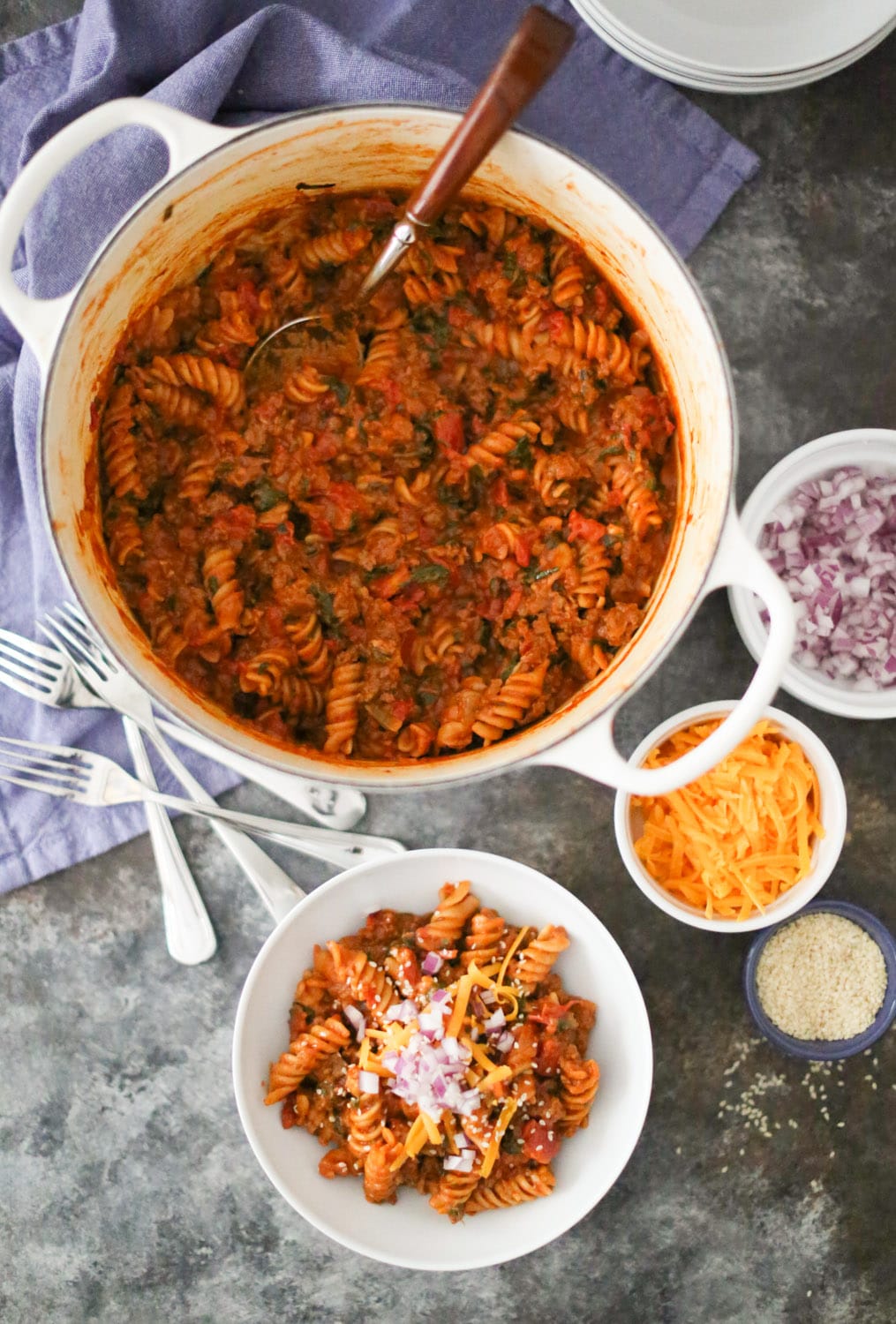 Large pot of cheeseburger pasta with a serving spoon and one garnished portion in a bowl.