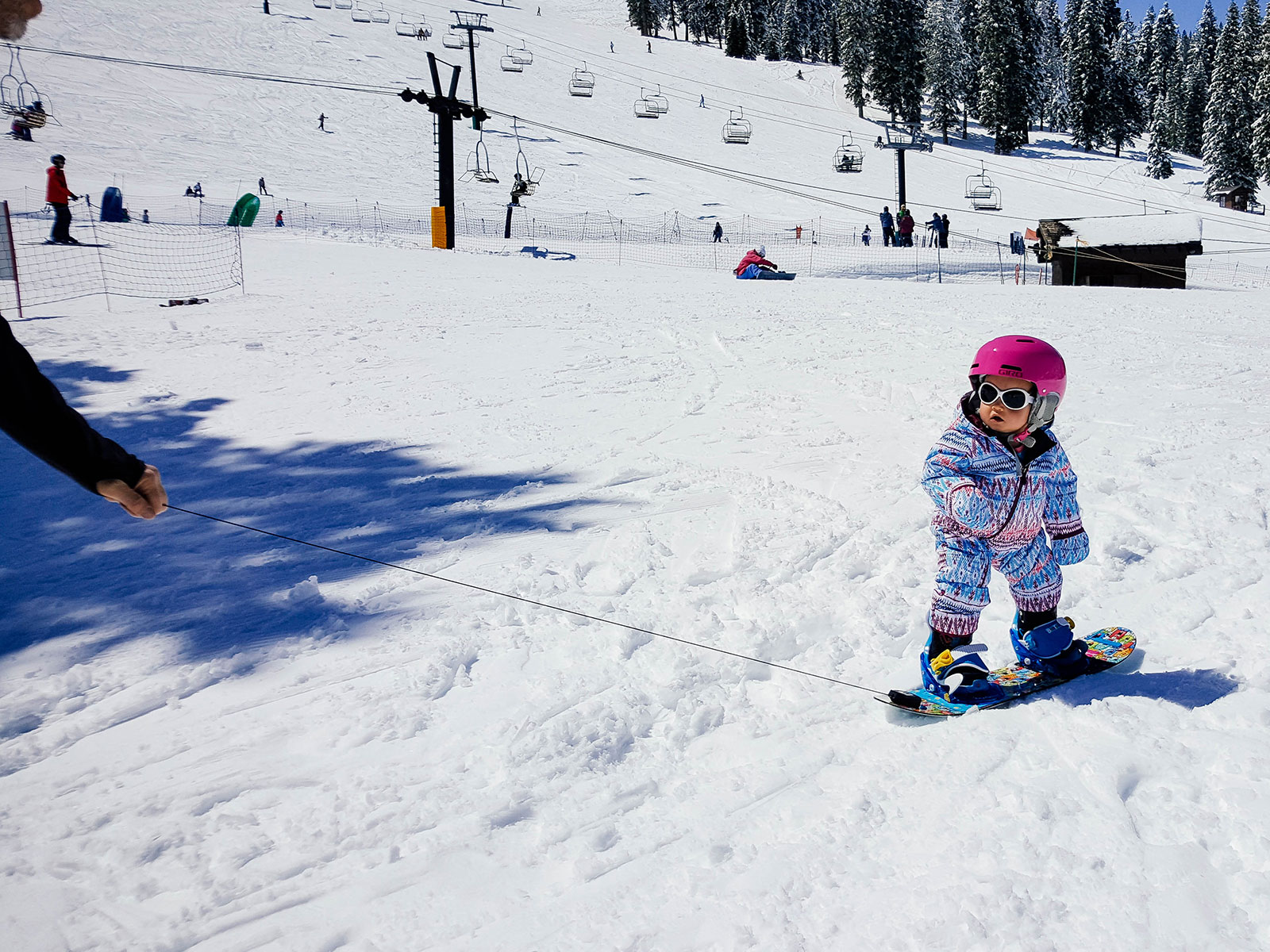 A 1-year-old baby being towed around on a snowboard with the Burton Riglet Reel