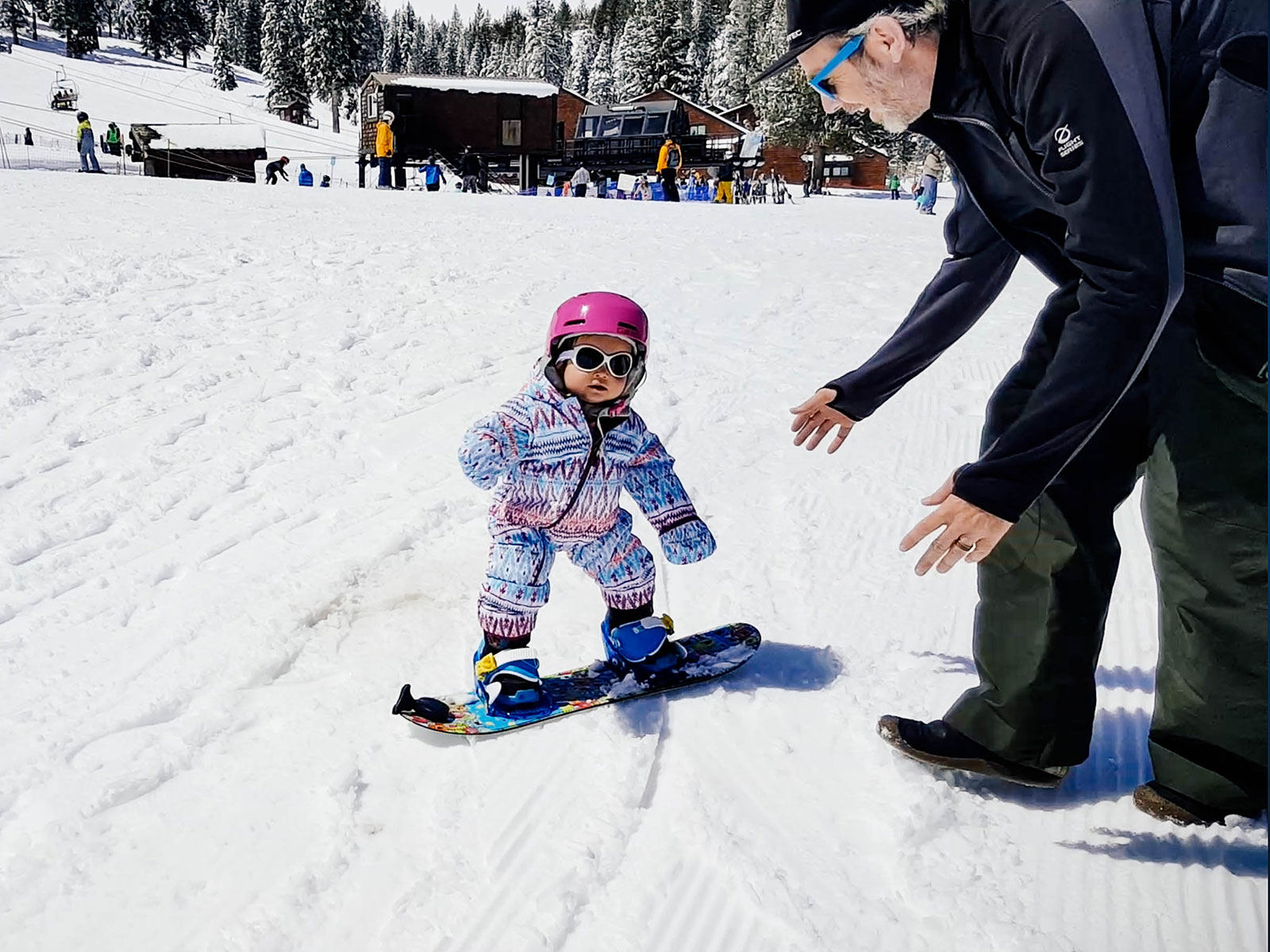 A 1-year-old learning how to snowboard on the bunny hill