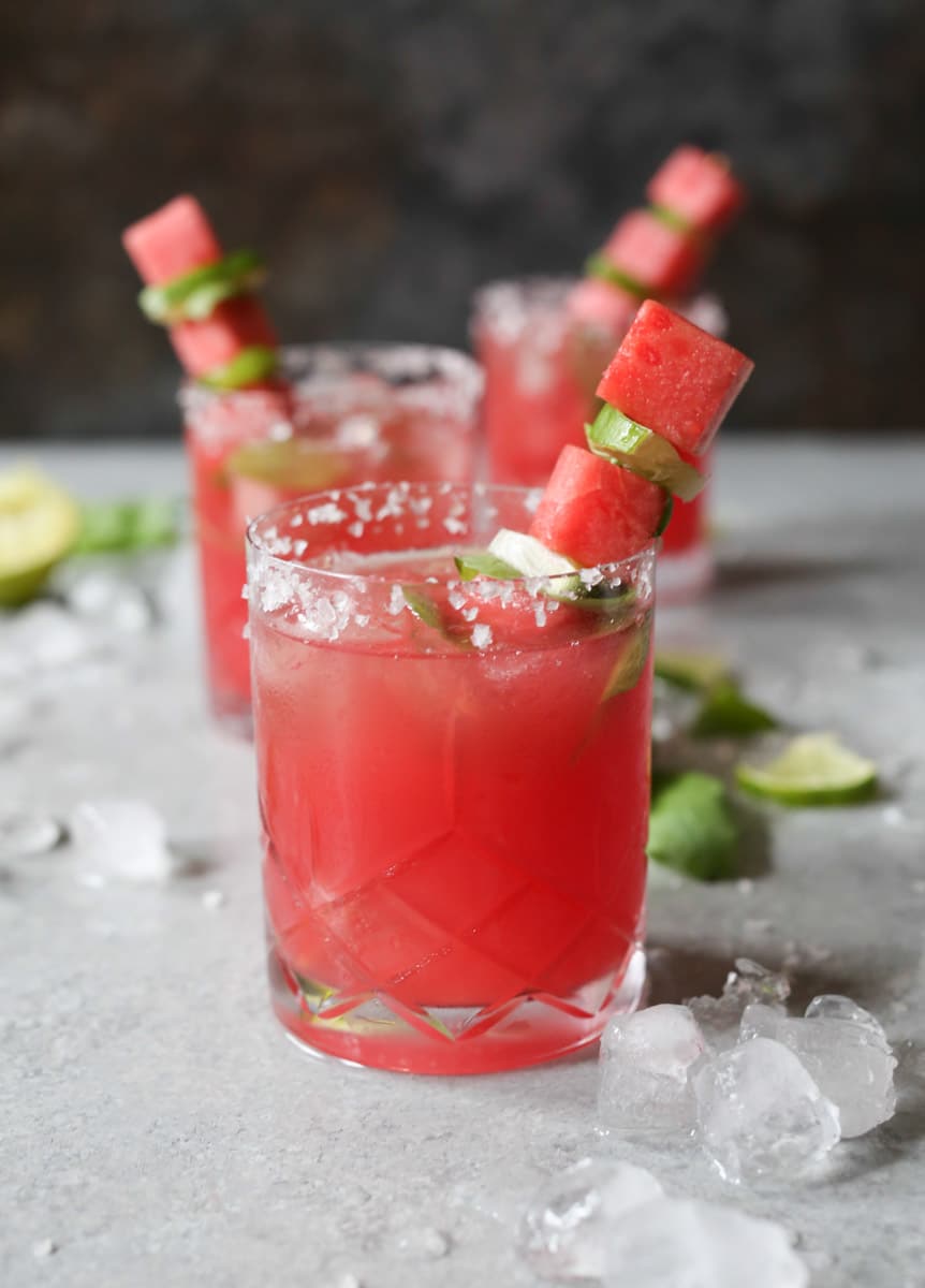 Two glasses of Watermelon-Basil Margarita garnished with skewers of watermelon and lime. 