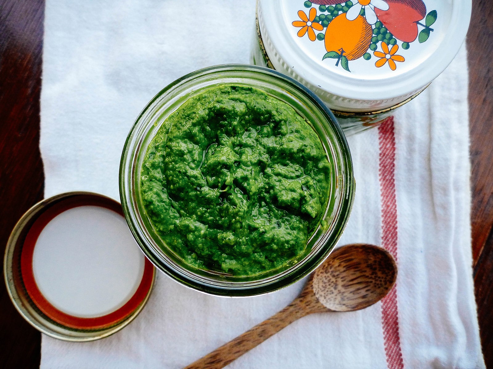 Overhead shot of jar of nasturtium pesto with a wooden spoon next to it