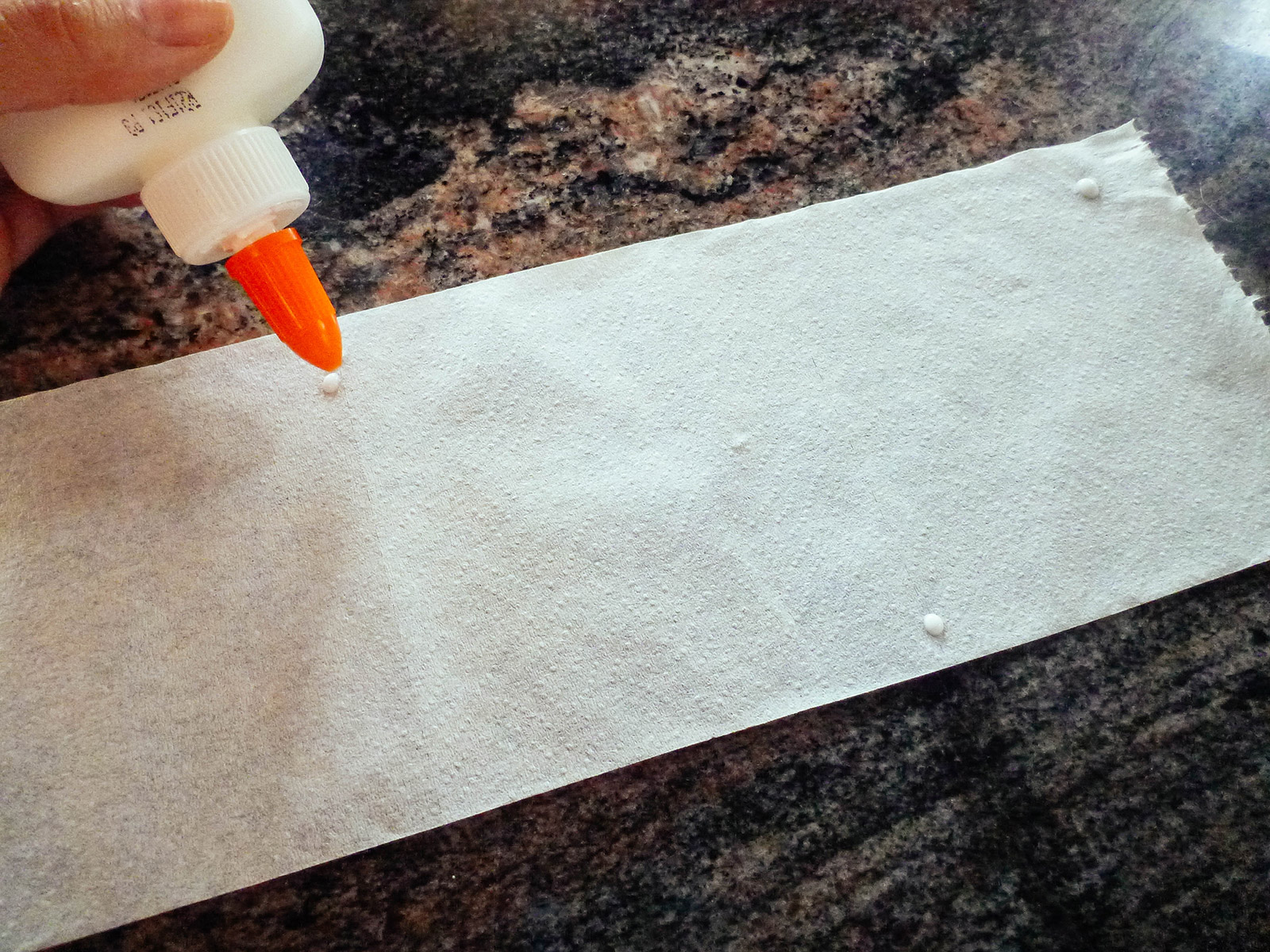 Drops of glue from a glue bottle being placed in a staggered row on toilet paper