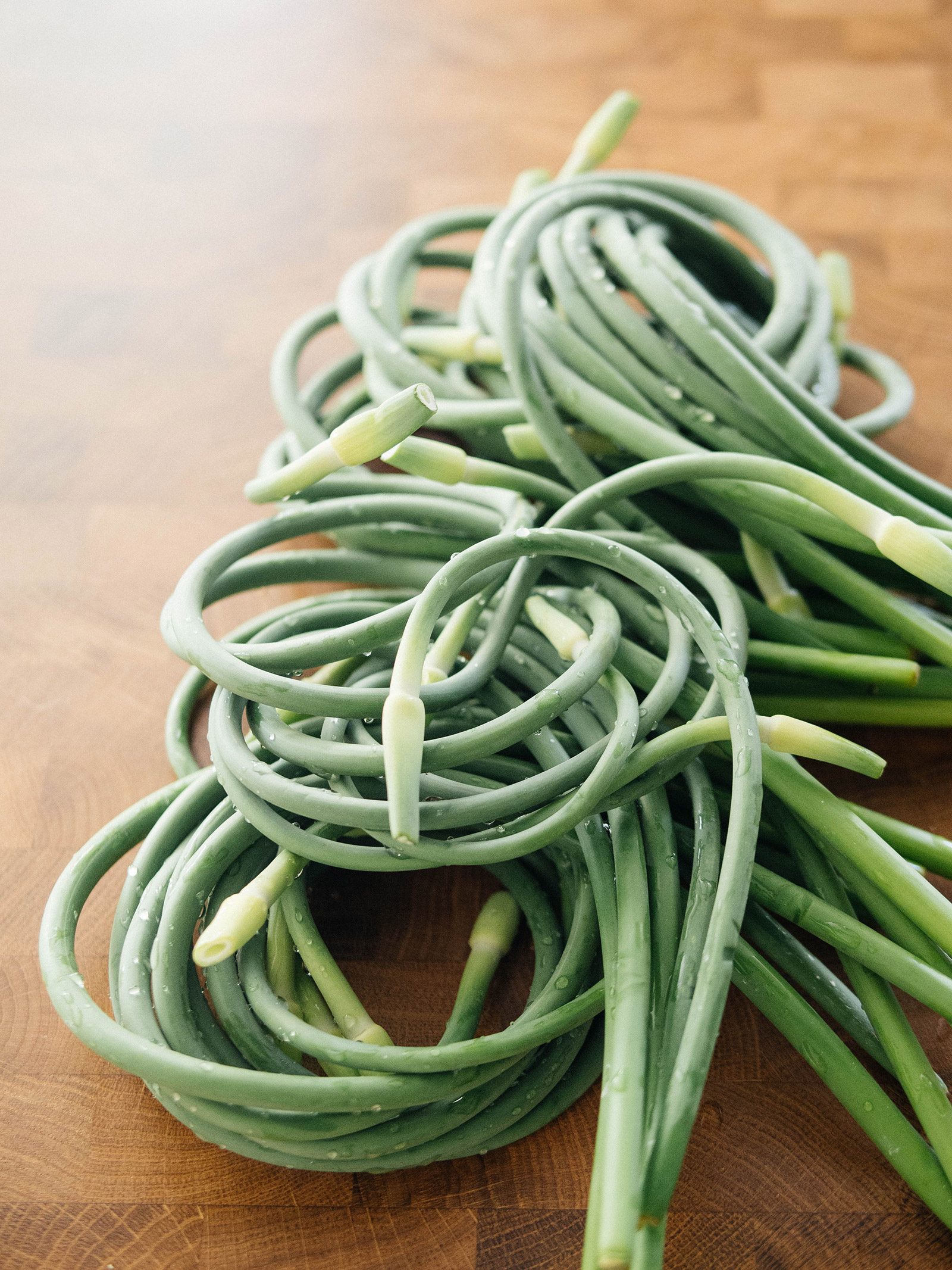 A pile of harvested garlic scapes on a butcher block counter