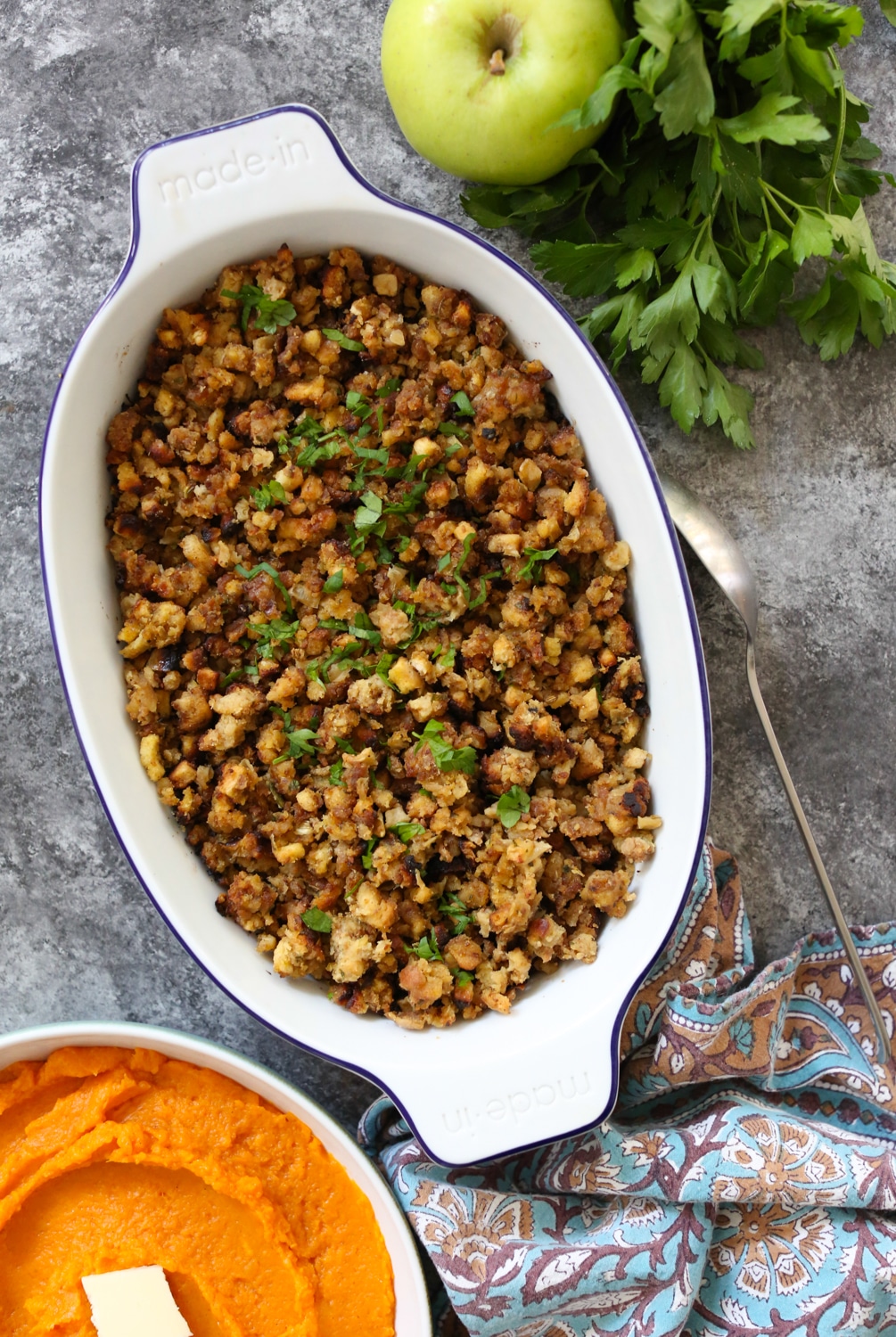 Overhead shot of stovetop stuffing in an oval baking dish on top of a colorful linen with a green apple and parsley in the corner.