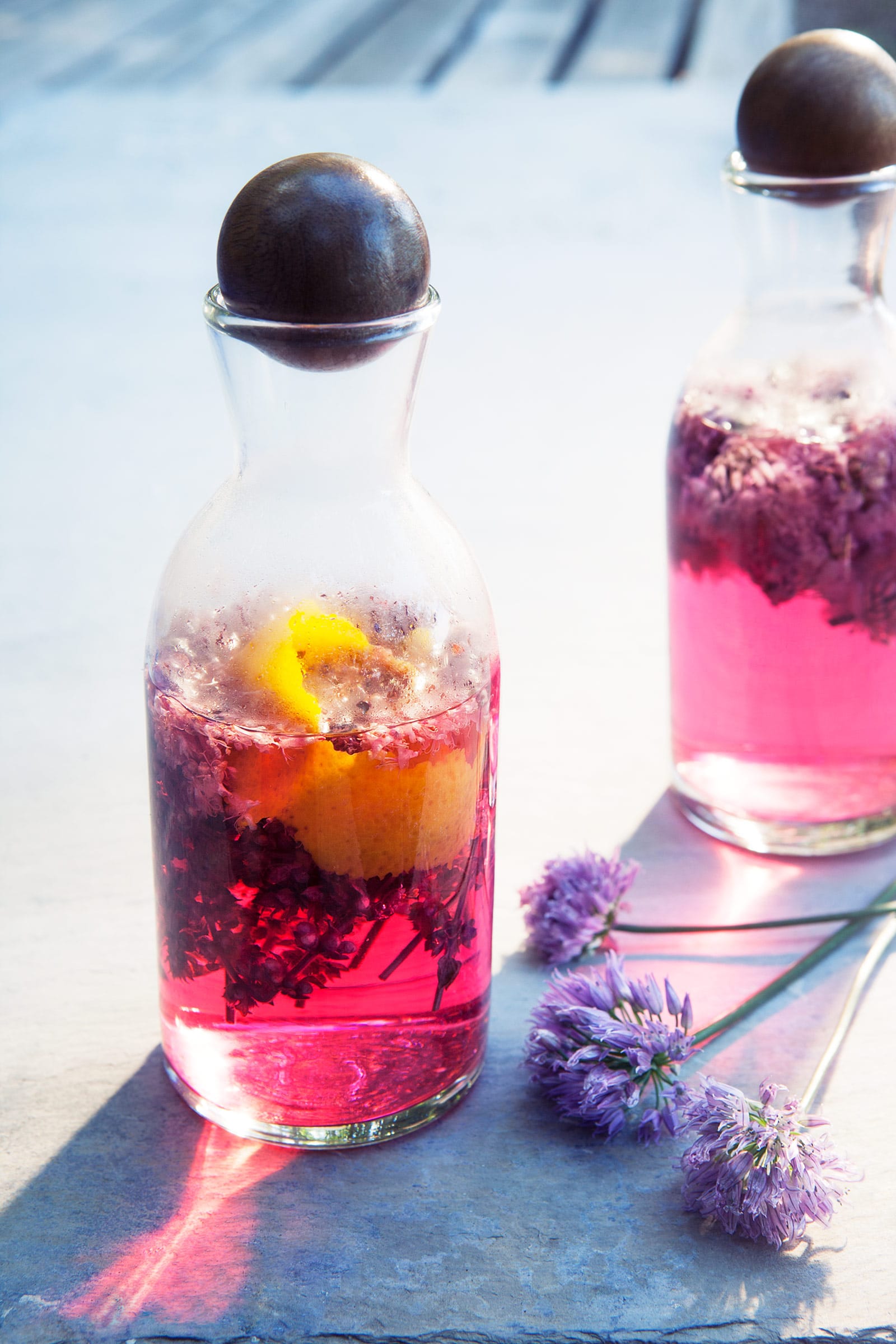 Two glass jars filled with pink-colored chive blossom vinegar on a concrete surface