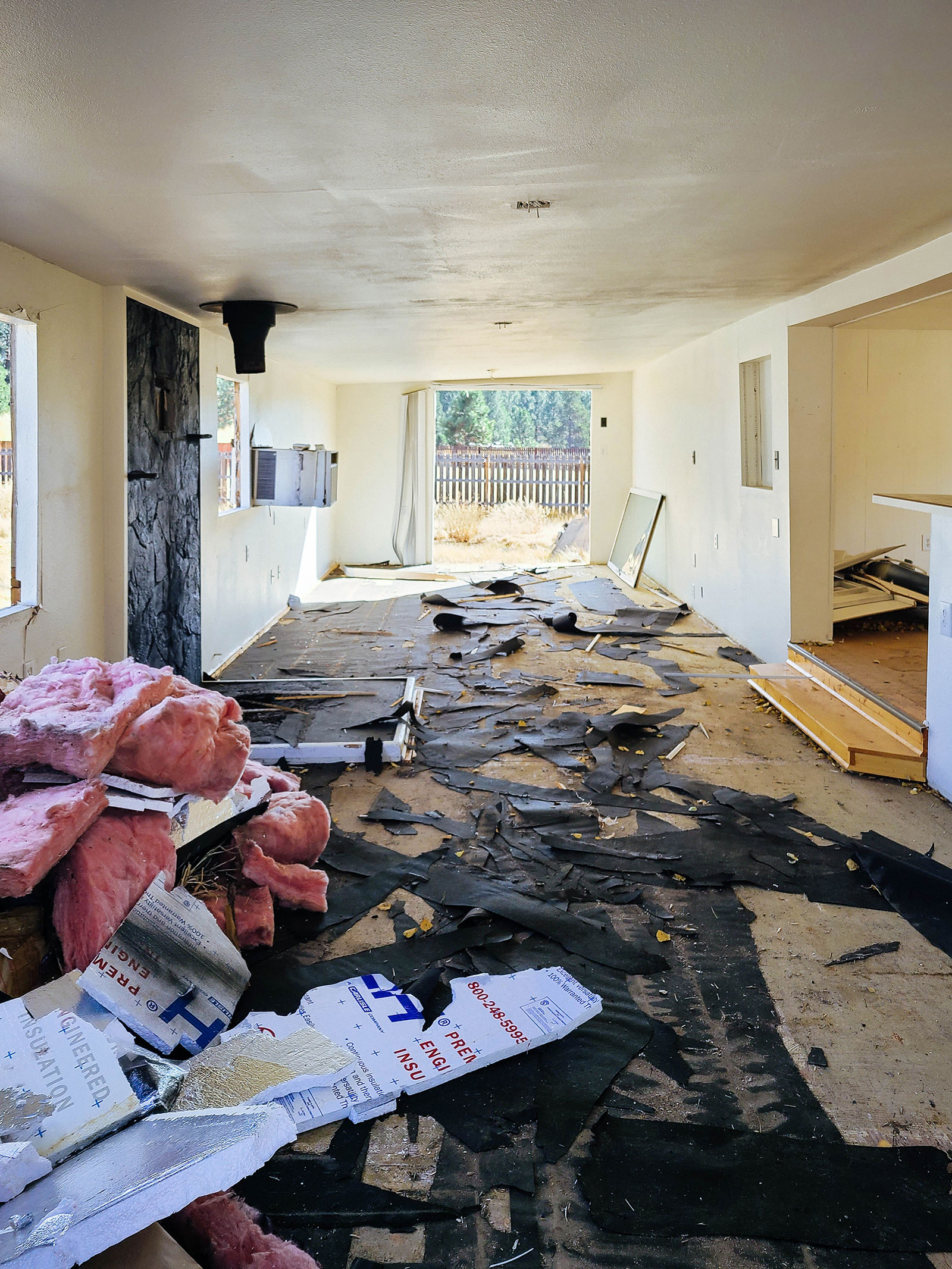 Interior shot of a gutted living room with old floor backing and pink insulation scattered in piles