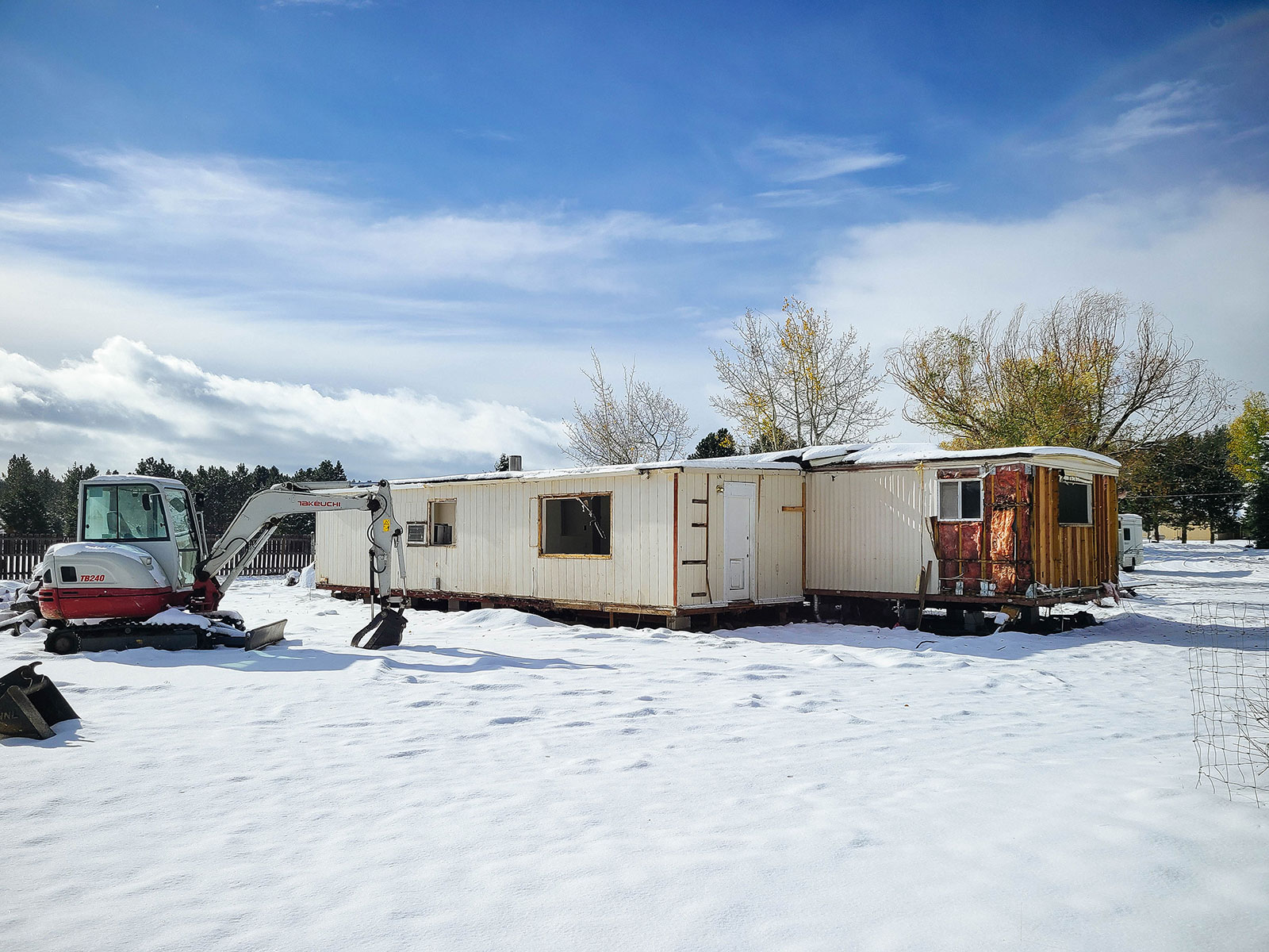 A mini excavator parked next to a beige mobile home with fresh snow on the ground
