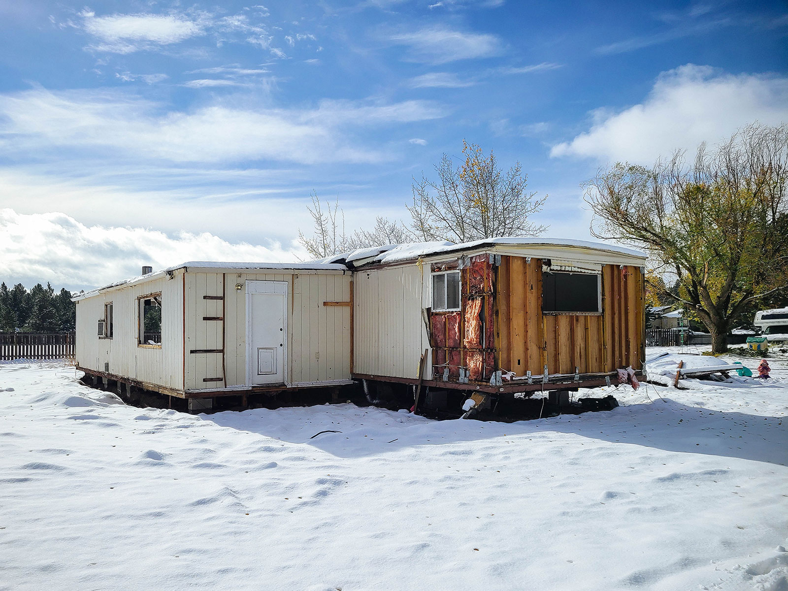 An older manufactured home with part of the siding removed, revealing pink insulation and wires