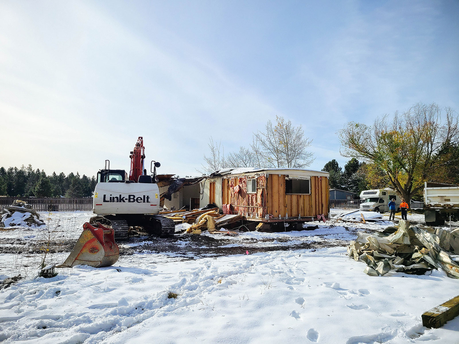 A large excavator demolishing an old home in a snowy yard