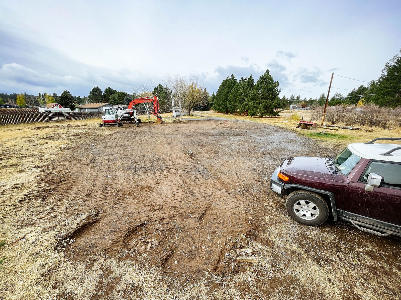 Burgundy SUV parked on a smooth and graded dirt lot with excavators in the background