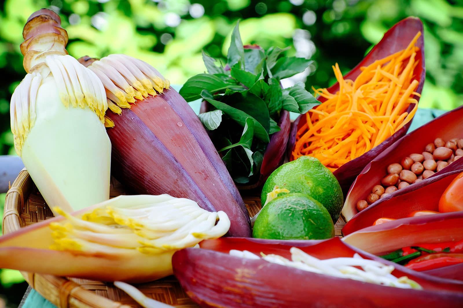 Salad ingredients portioned out in banana bract "bowls" with banana flowers on a straw tray