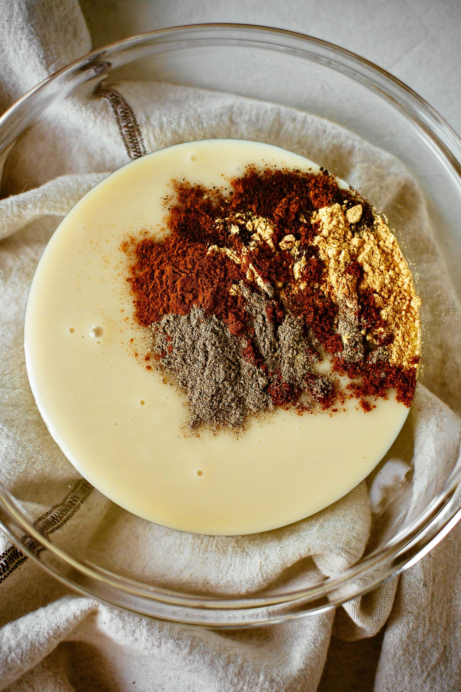 Various ground chai spices dropped in small spoonfuls in a glass bowl of condensed milk