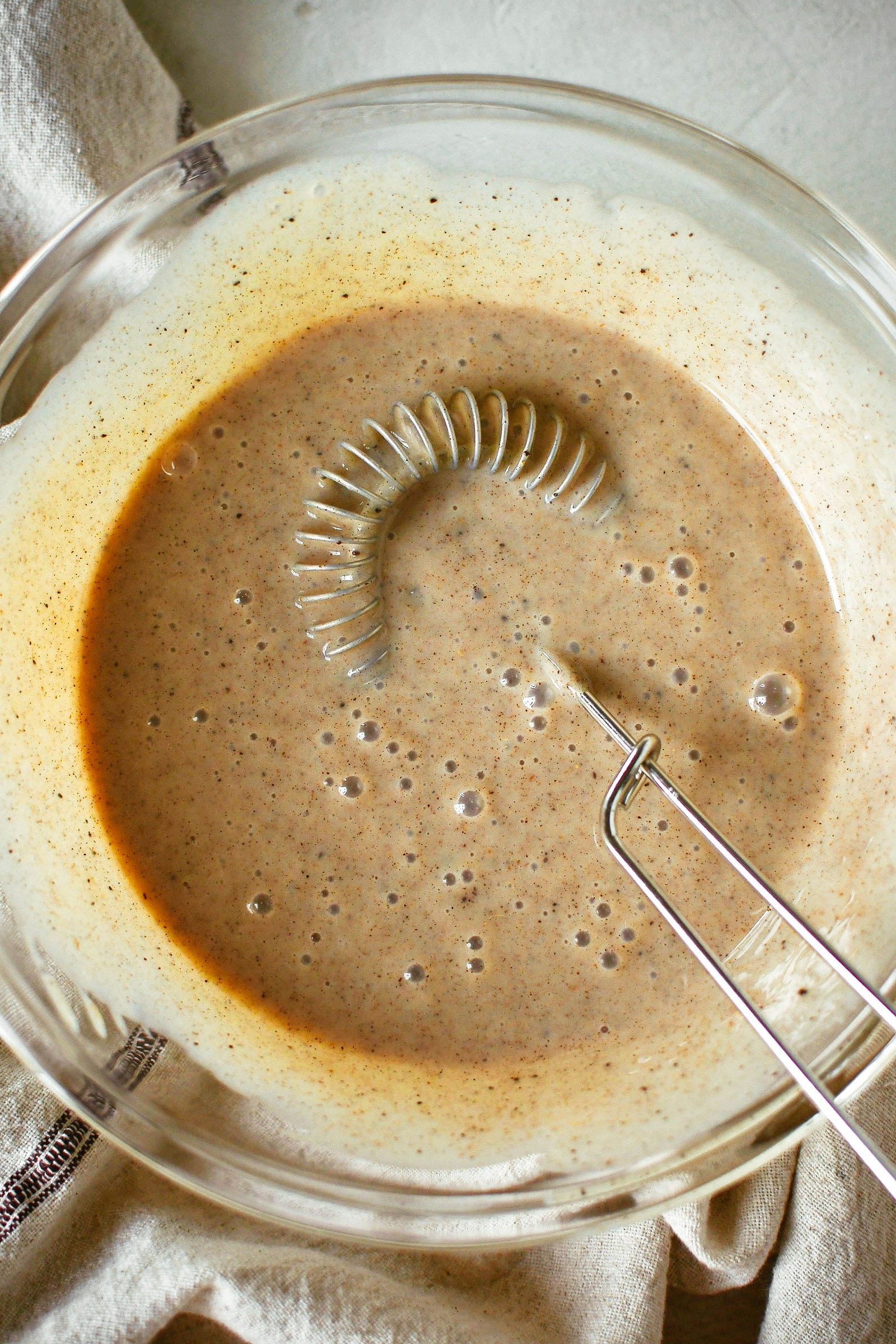 A whisk resting in a glass bowl of homemade chai concentrate