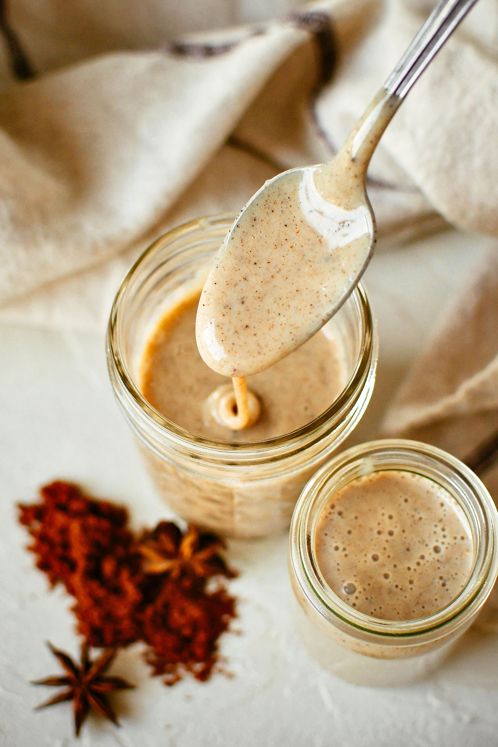 Closeup view of a spoonful of creamy chai concentrate liquid dripping down into a jar of more chai concentrate