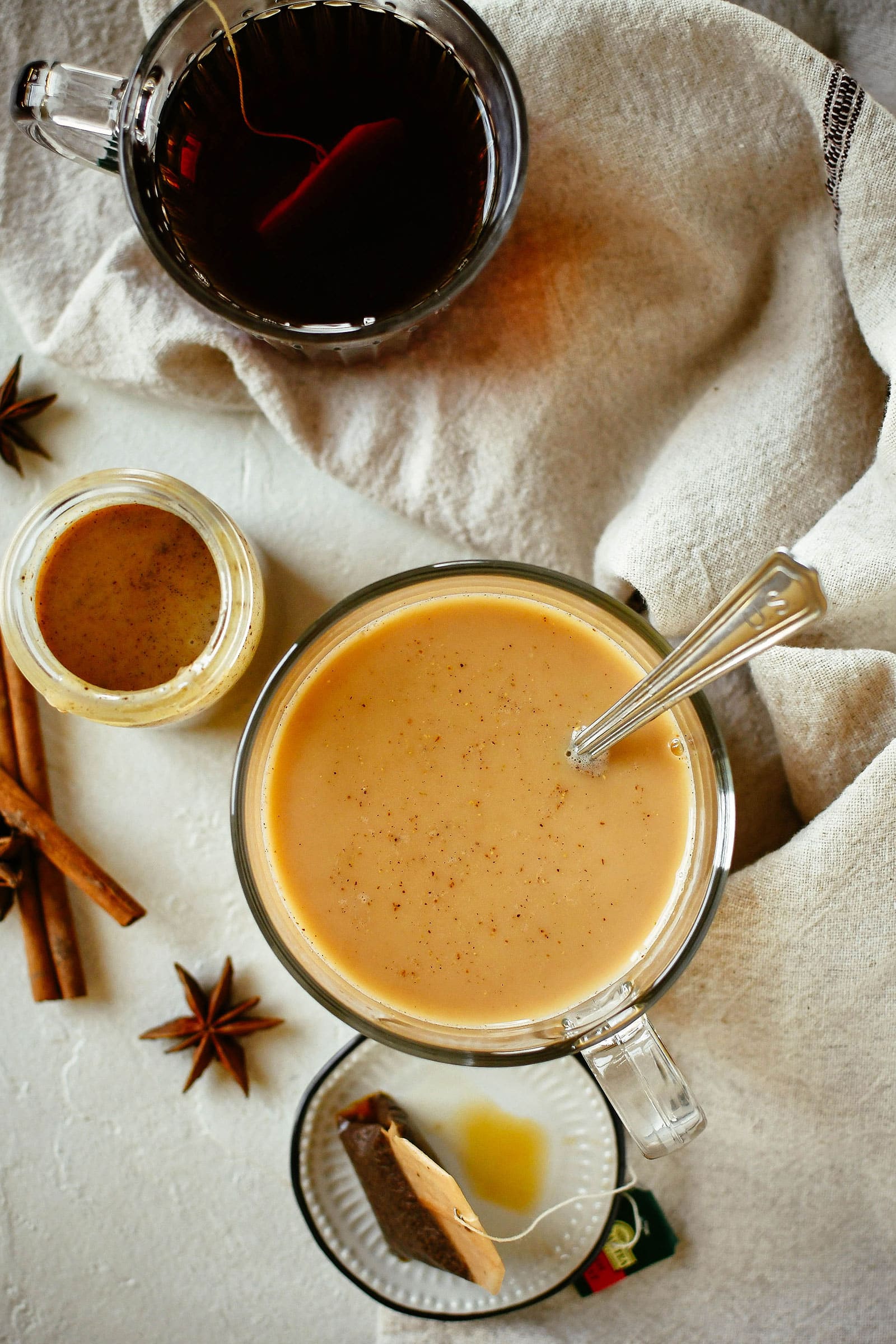 Overhead shot of a mug of hot tea next to another mug with creamy chai concentrate stirred into it