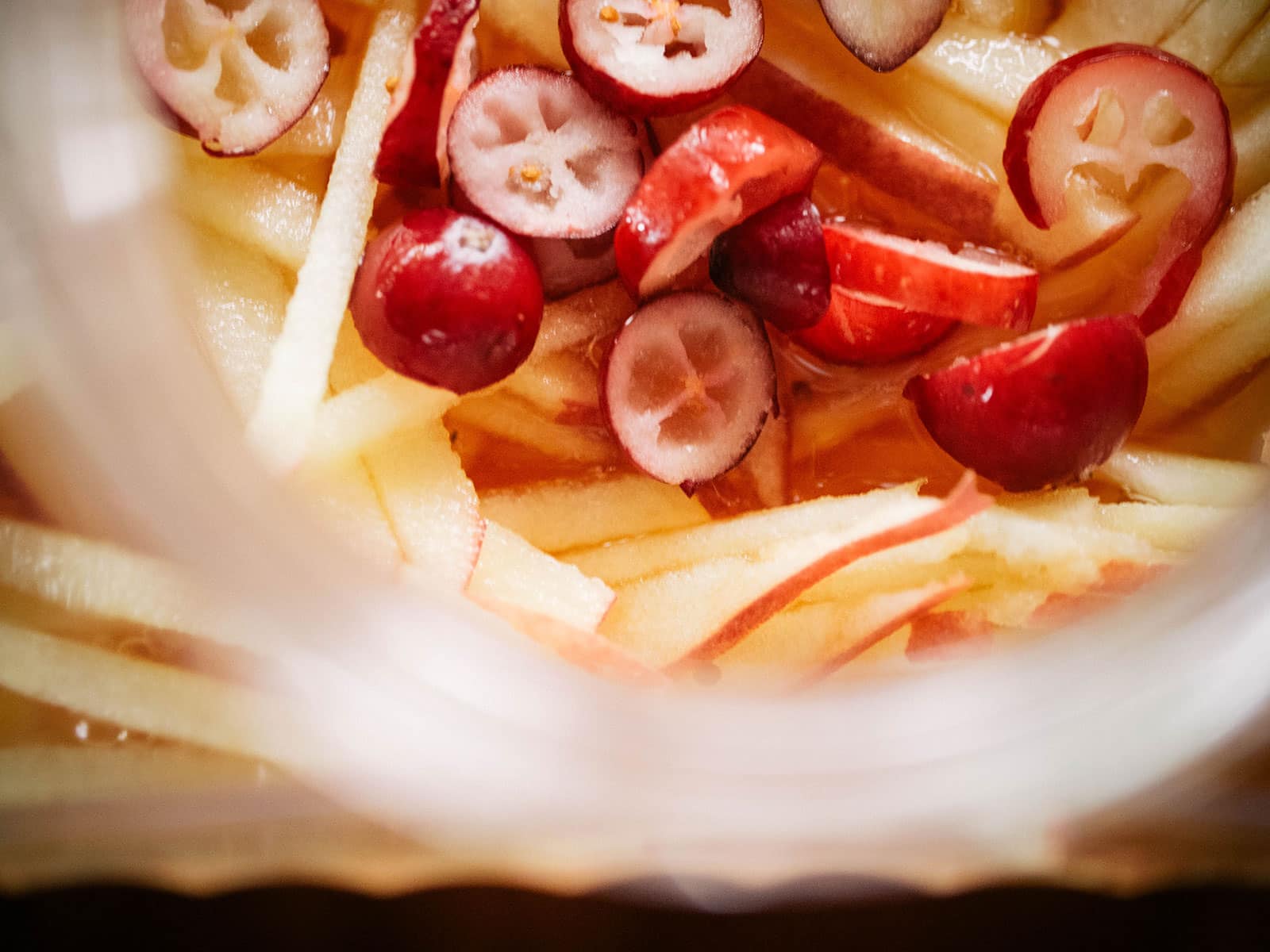 Overhead shot of sliced cranberries and apple matchsticks floating in white wine in a glass pitcher