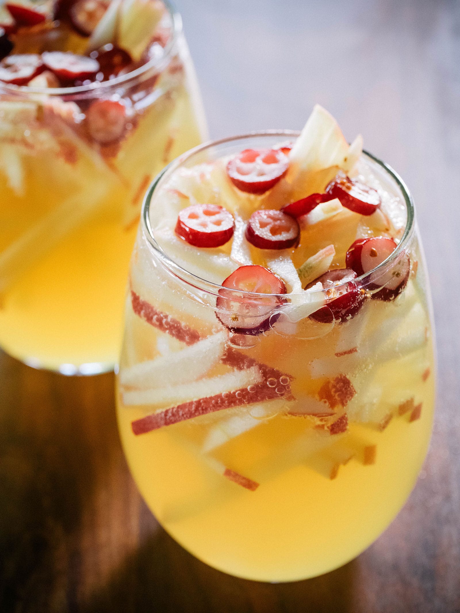 Two stemless wine glasses filled with sparkling apple cider sangria with sliced cranberries on top