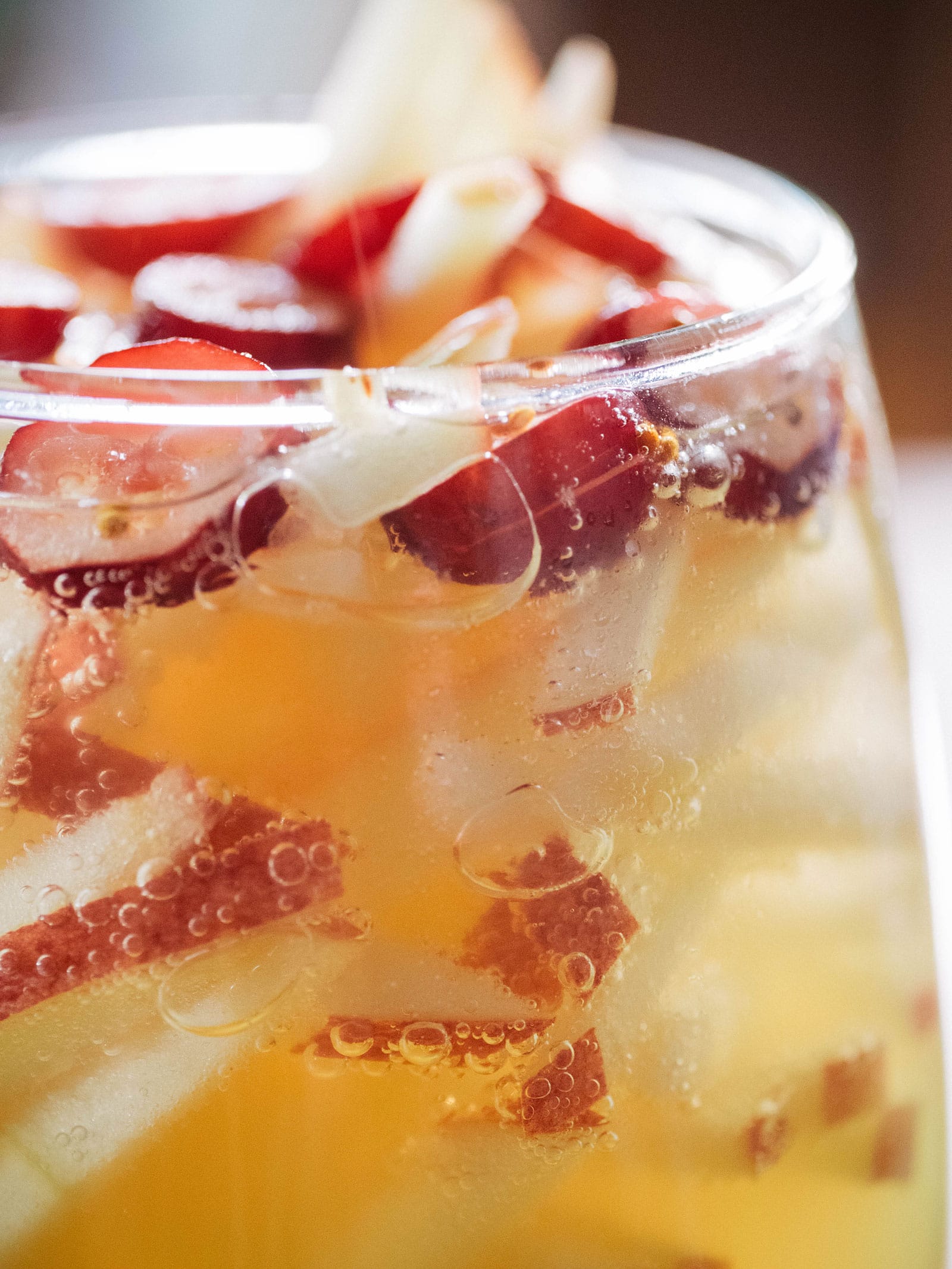 Macro shot of fizzing bubbles, sliced cranberries, and apple matchsticks in a glass of sparkling apple cider sangria