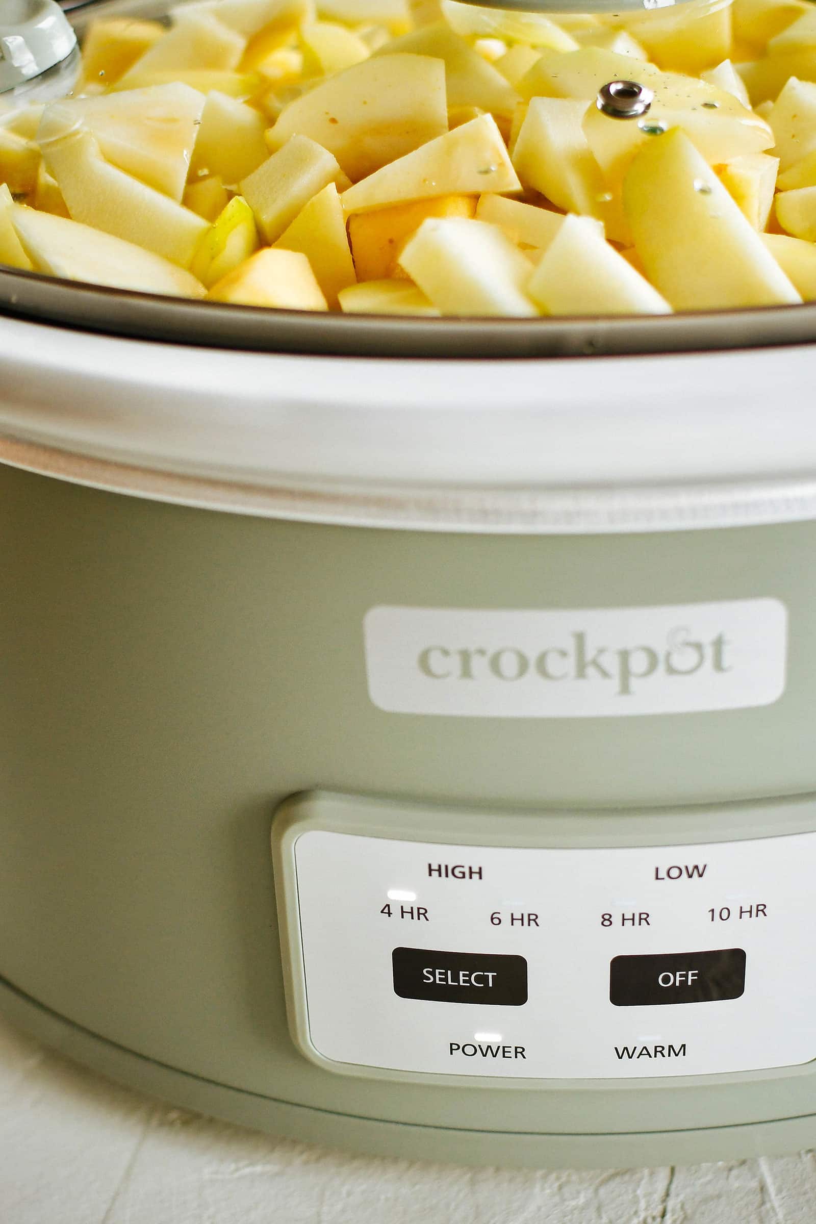 Close-up of a green crockpot with chopped apples and pears, set on high for four hours