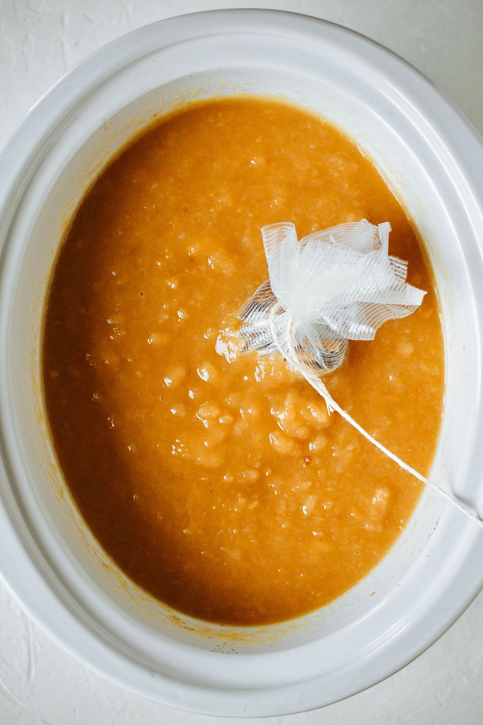 Overhead shot of crockpot filled with an apple-pear mixture and a spice sachet