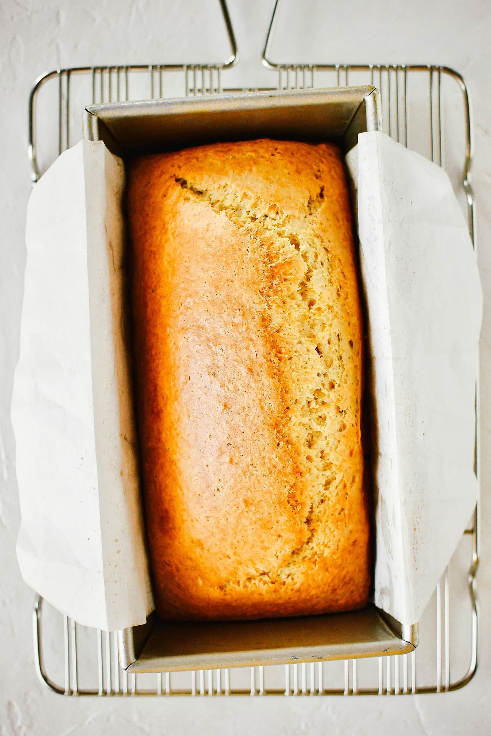 Fresh baked grapefruit-rosemary bread in a parchment-lined pan, cooling on a rack
